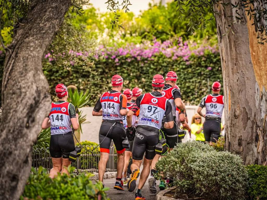 Competitors in the Swimrun Côte d’Azur running on the paths of Beaulieu-sur-Mer, race bibs on their backs and swim paddles in hand (photograph from the 2025 edition): the tenth edition takes place this Sunday 18 October between Beaulieu, Saint-Jean-Cap-Ferrat and Villefranche-sur-Mer.